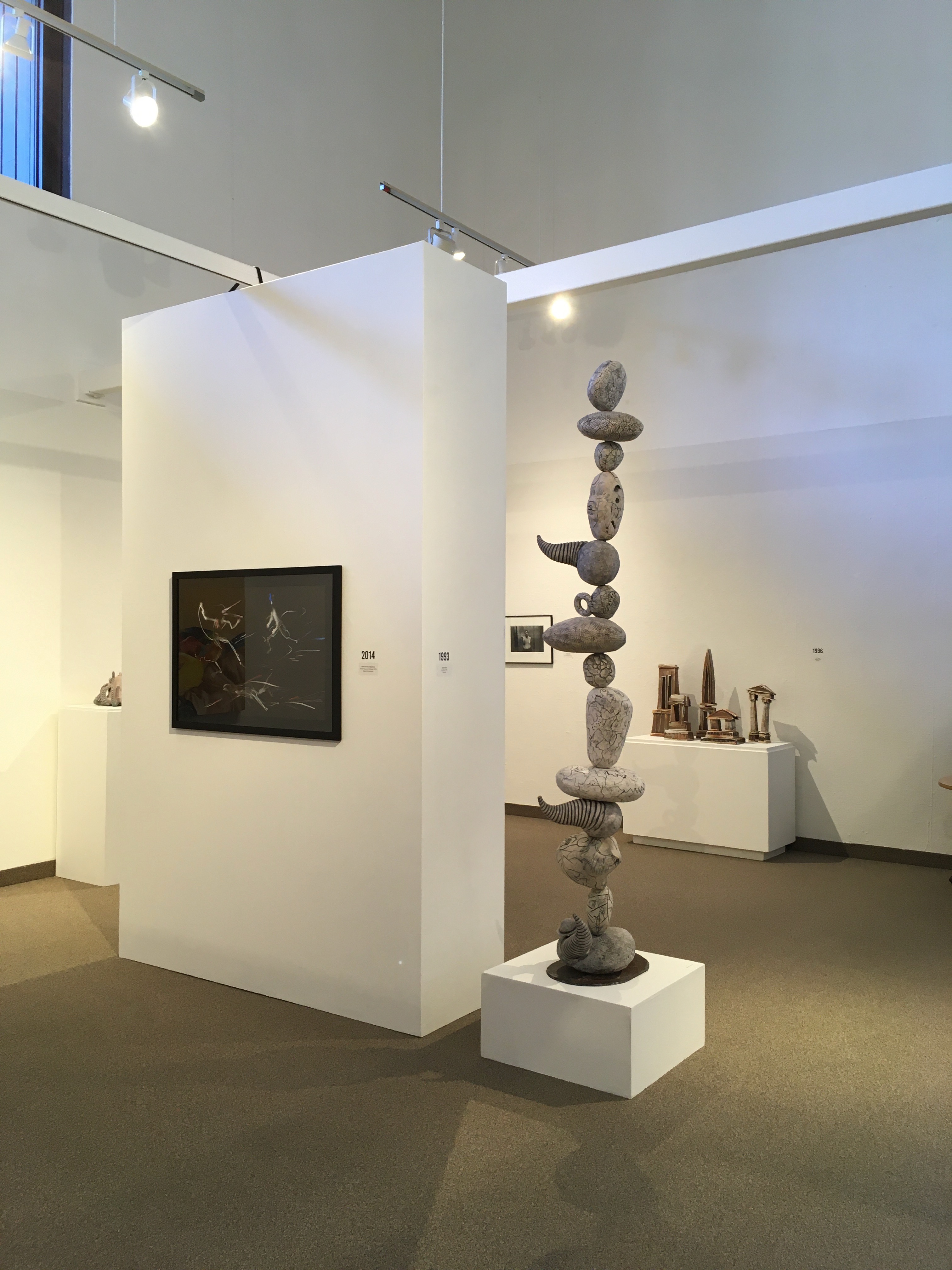 view of a sculpture of stacked ceramic organic shapes, a white wall with a photograph on it