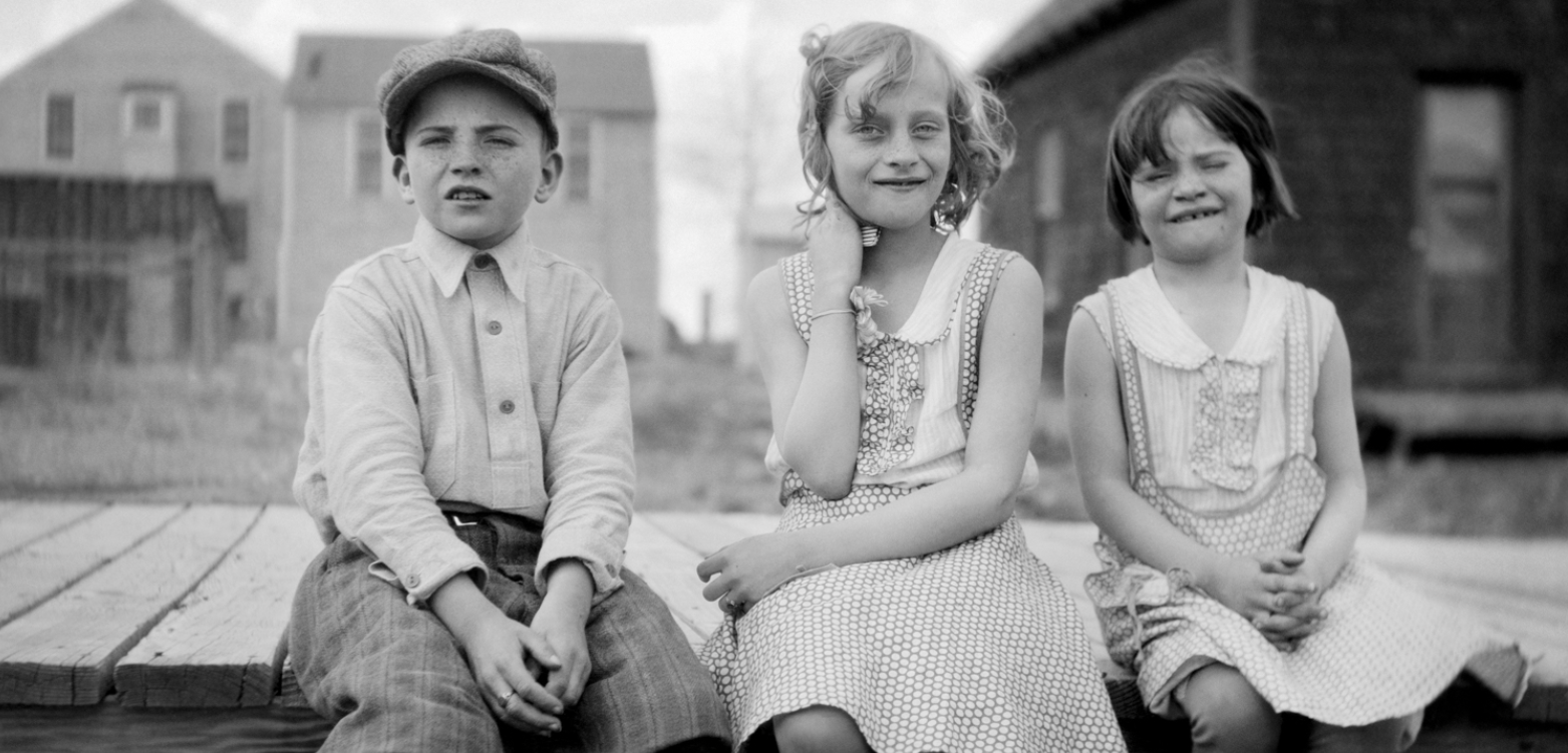 black and white photo of three children looking into the camera, sitting outside on a flatbed truck